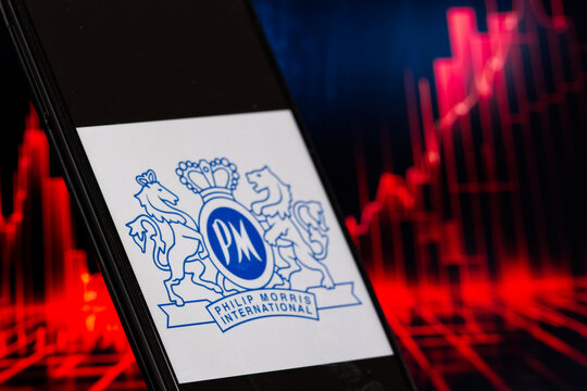 PM Philip Morris logo displayed on a smartphone screen against the background of a stock red chart on a computer screen.