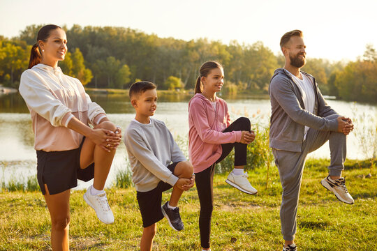 Fit and active happy parents with two kids boy and girl doing sport exercises in nature. Smiling family in sportswear having workout in the park. Outdoors training and fitness concept.