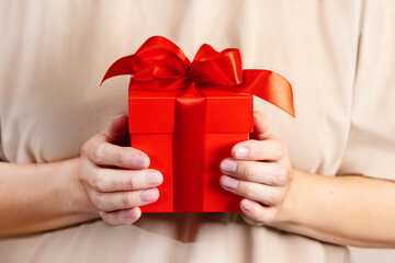 A woman's hands holding a gift with a red bow close up