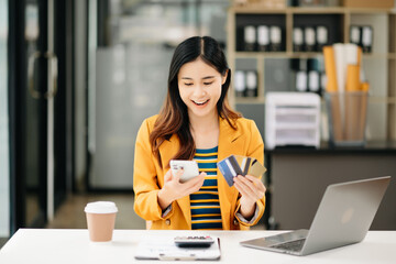 Asian Woman using smart phone for mobile payments online shopping, omni channel, sitting on table,...