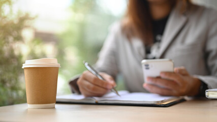 A paper cup of coffee on wooden office desk with businesswoman sitting on background