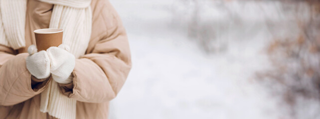 Female hands holding coffee hot drink cup and enjoys winter weather at snowy street close up with copy space mockup
