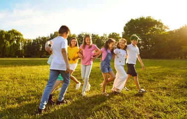 Fotobehang Group of a playful kids friends playing active outdoor games on a green grass in the summer park. Happy children having fun outside on a sunny day in the camp. Summer holiday concept. © Studio Romantic