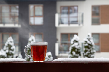 glass cup of tea in snow on balcony in winter