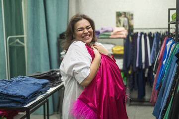 Caucasian fat woman looks excitedly at a festive pink dress in a store. Plus size. 