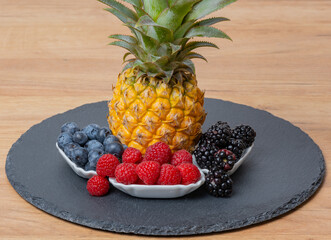 Ananas Frucht mit Himbeeren, Brombeeren und Heidelbeeren auf einer Schiefertafel