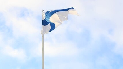 Video of Finnish flag blue cross on a white field flying on a flagpole against a blue sky with sun and clouds