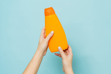 Packaging of shampoo or conditioner in woman's hand on blue background. Copy space and mock up - obrazy, fototapety, plakaty