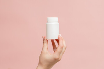 White bottle (plastic tube) in hand on pink background. Packaging for vitamins, pill or capsule, or...