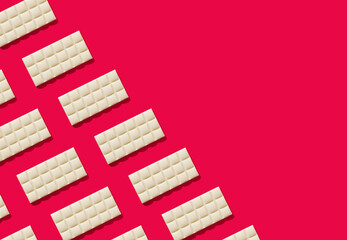 Trendy pattern made of white chocolate on red background. Minimal concept. Yummy sweet food idea. Creative chocolate bars composition. White chocolate aesthetic background. Flat lay. Copy space.