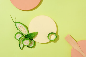 On a green background with color podiums, fresh bitter melon slices decorated. Blank space for display product. Vitamin E in the bitter gourd mask helps to hydrate and soften the skin