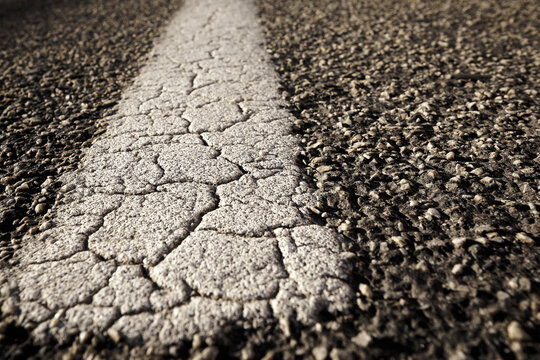 Alte marode rissige Fahrbahnmarkierung auf einer Stra&szlig;e aus Asphalt