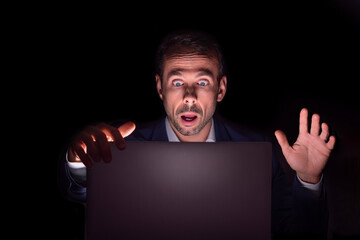 Businessman staring at laptop with frightened face in the dark