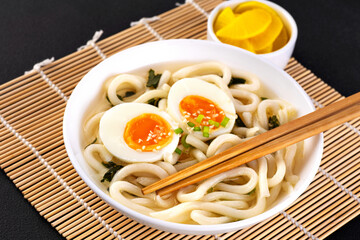 Asian vegetarian udon noodles soup with boiled eggs, wakame seaweed and sesame seeds.