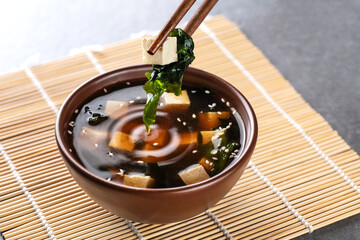 Japanese miso soup in a brown bowl. Chopsticks take tofu and wakame seaweed. - obrazy, fototapety, plakaty