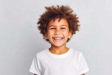 Cute mixed race boy child model with perfect clean teeth laughing and smiling, happy. Curly hair and white shirt, healthy. Isolated on white background. - obrazy, fototapety, plakaty