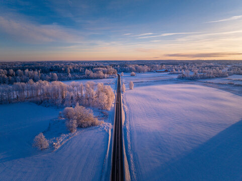 Winter Wonderland Sunrise: Majestic Aerial View of a Swedish Landscape with a Serene Roadway Cutting Through the Frozen Beauty