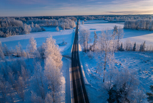 Winter Wonderland Sunrise: Majestic Aerial View of a Swedish Landscape with a Serene Roadway Cutting Through the Frozen Beauty
