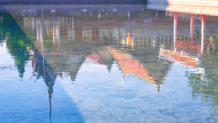 Beautiful light reflection background of Thai temple against blue sky on water surface in the pond.