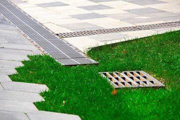 pavement with stone tiles decorative pattern and trimmed green lawn on summer park with drain...