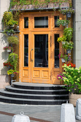 Fototapeta na wymiar Wooden door with granite enter, building architecture decorated with flowers in flowerpots on summer day.