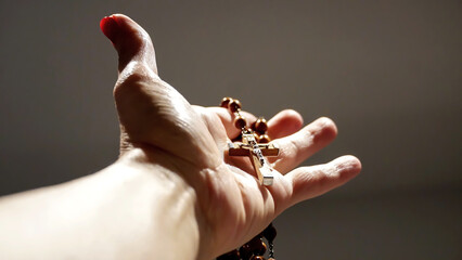 A rosary and it's cross are held in one hand, with dramatic lights on an isolated background  - obrazy, fototapety, plakaty