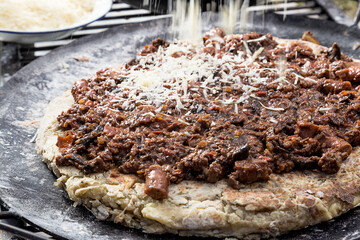 Pasta a la parrilla con salsa de salchicas y carne picada, con queso rayado cayendo, sobre una bandeja de metal 
