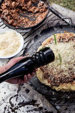 Manos Condimentando con un molinillo pimentero, pasta a la parrilla con salsa y queso rayado en una fuente de acero