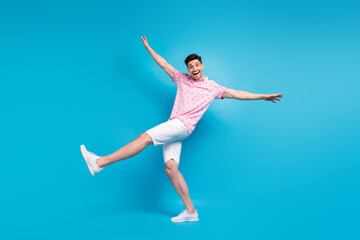 Full size portrait of cheerful overjoyed young man good mood raise arms dancing isolated on blue...