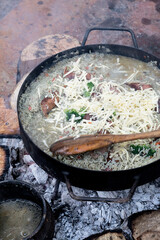 Arroz cocinandose en caldo, con queso rayado y un cucharon de madera, al disco sobre un fogonero...
