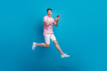 Full size profile portrait of astonished person jump use smart phone empty space isolated on blue color background