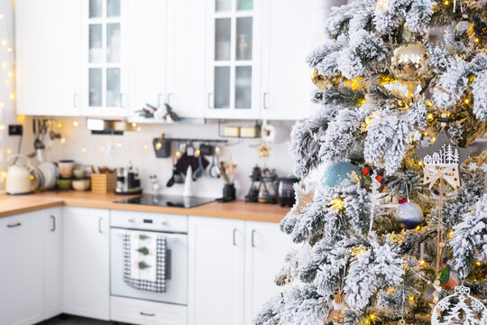 Festive Christmas decor in white kitchen, modern rustic interior with a snowy Christmas tree and fairy lights. New Year, Christmas mood, cozy home. The general plan