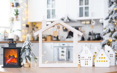 Key and tiny house of a small size on cozy home with Christmas decor on table of festive white kitchen. Gift for New Year. Insurance, moving to new house, mortgage, rent and purchase real estate