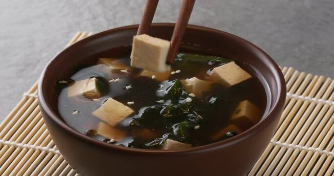 Japanese miso soup in a brown bowl. Close-up footage on the rotating table. Chopsticks take tofu.