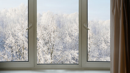 View from the window on a winter landscape with blue sky,  trees and falling snow.