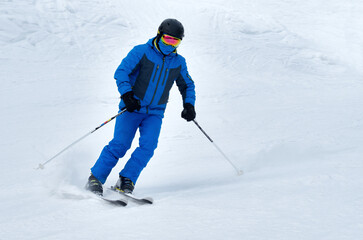 Fototapeta na wymiar A man in blue sportswear on skis rides down a snowy slope