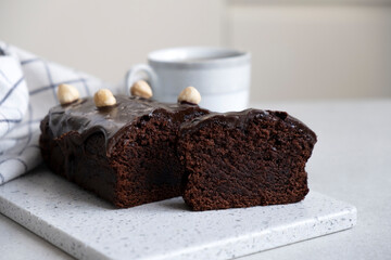 Chocolate pound cake with chocolate ganache on kitchen board with towel and cup of tea or coffee....