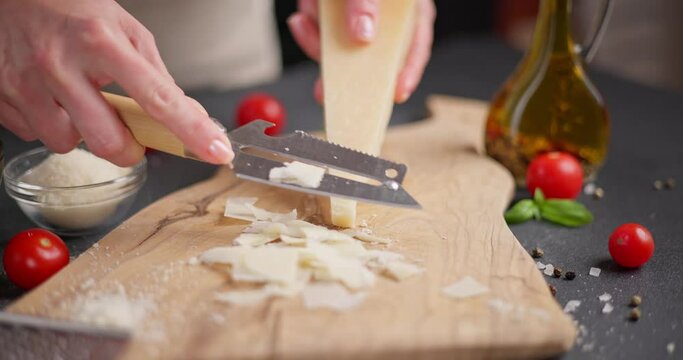 Woman slicing Piece of Traditional Italian Parmesan Hard cheese into flakes on a wooden cutting board at domestic kitchen
