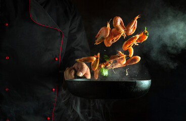 A professional chef cooks shrimp in a hot frying pan with steam. Concept of cooking seafood or...