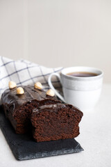 Chocolate pound cake with chocolate ganache on slate board with kitchen towel and cup of tea or coffee. Homemade bakery dessert, classic recipe of chocolate loaf cake.