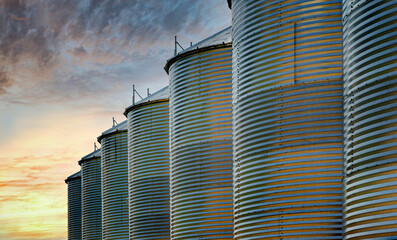 Row of grain silos silhouetted against a sunset © Wirestock