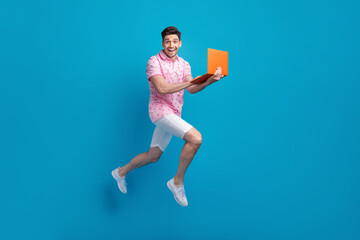 Full size profile portrait of overjoyed sporty guy jump rush use netbook isolated on blue color background