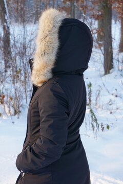 Kobieta w czarnej kurtce (Anorak). Duży, ciepły kaptur założony w lesie podczas zimowej pogody.