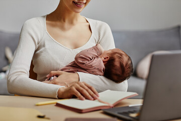 Close up shot of joyful mom working at home office with napping baby in arms, copy space