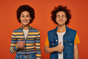 cheerful african american siblings in vibrant outfits posing together on orange background, family
