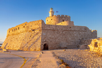 Old stone lighthouse illuminated by the sun at Fort St. Nicholas in Rhodes early in the morning.