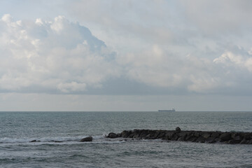 Fototapeta premium A cargo ship on the horizon at sea, cloudy weather and calm sea surface. Cargo delivery by sea, marine logistics