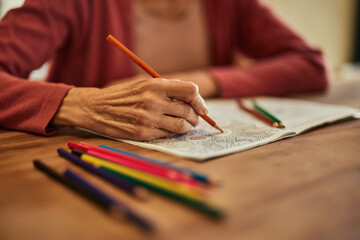 Close-up of a mature woman using crayons and coloring the coloring book.