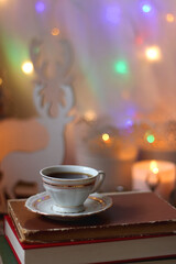 Bowl of cookies, cup of tea, dry oranges, pine cones, books, reading glasses, small presents, various Christmas decorations and lit candles on the table. Cozy Christmas hygge. Selective focus.