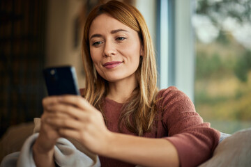 A close-up of a smiling woman, holding and using a mobile phone.